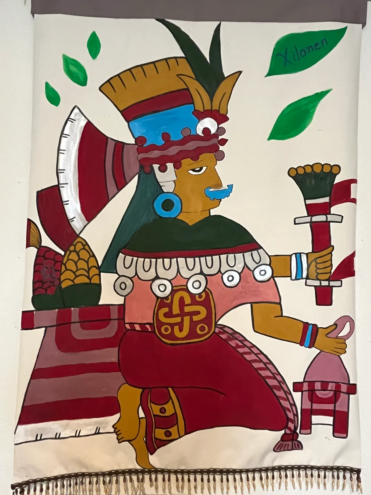 Hand-painted textile banner depicting an Indigenous ceremonial figure with ornate regalia and symbolic motifs.
