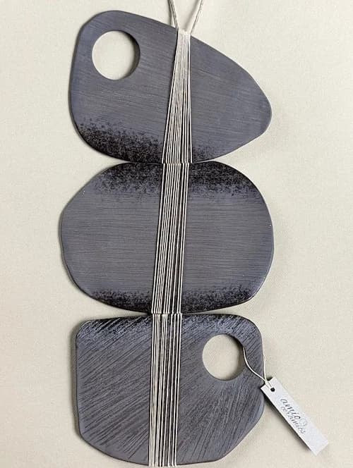 Abstract metal pendant with three organic forms connected by wire, featuring circular cutouts and textured surfaces.