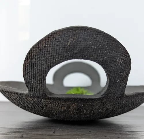 Abstract textile sculpture with curved form and open aperture, revealing a glimpse of green plant.