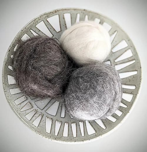 Three felted wool spheres nested in a geometric concrete vessel, exploring form and texture.