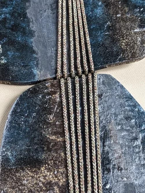 Abstract fiber artwork combining indigo-dyed textiles and twisted cord in geometric composition.