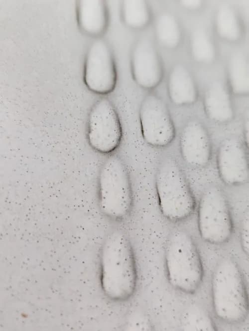 Abstract stone relief sculpture with repeated teardrop forms and textured surface.