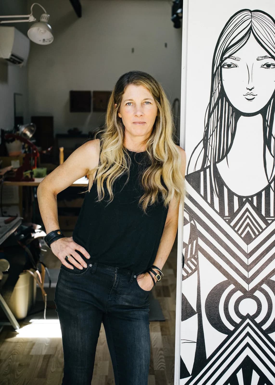 Artist posed next to a finished ink-and-line portrait drawing in a studio setting.