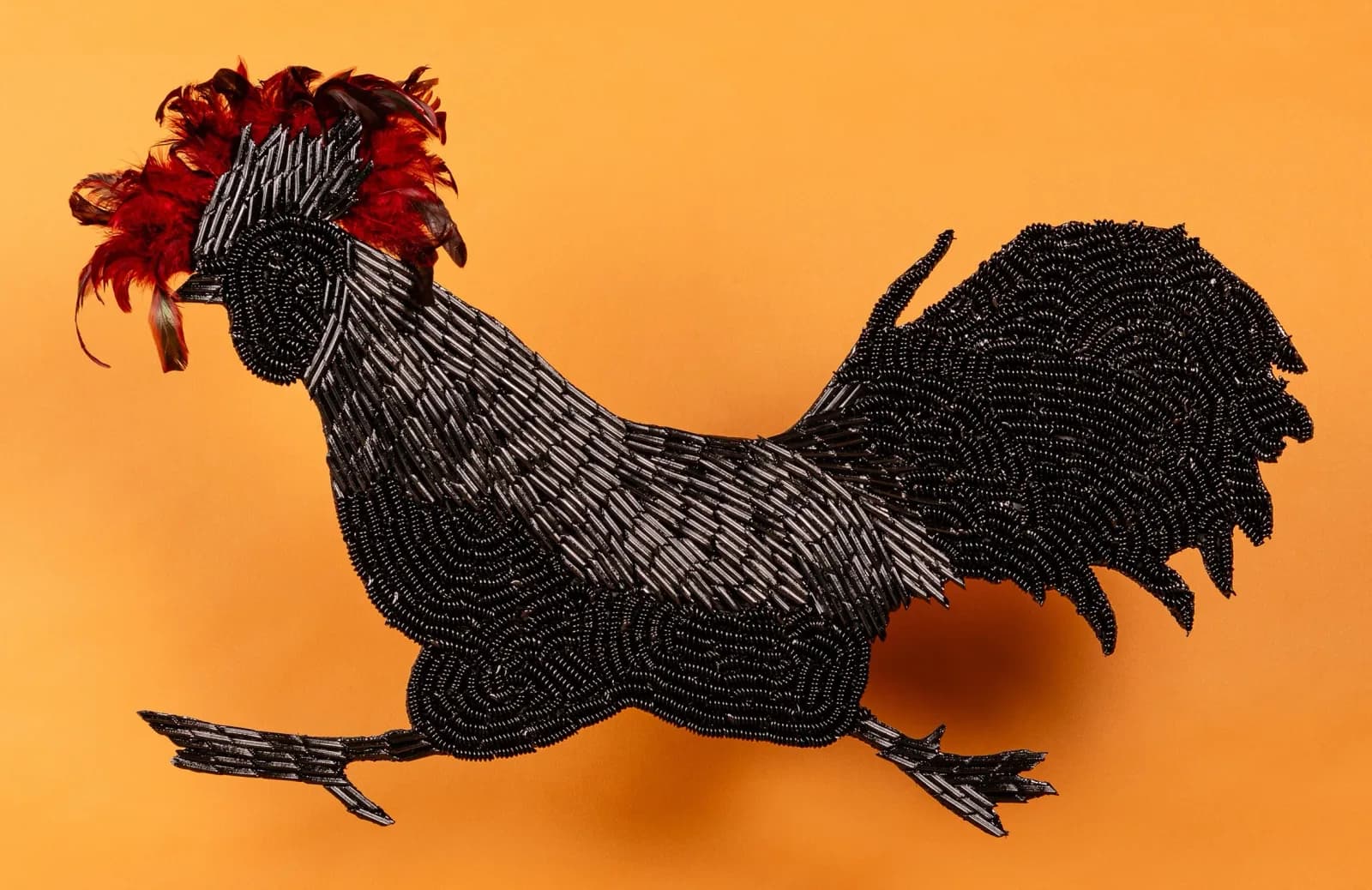 Black beaded rooster with red feathered comb on golden-yellow background.