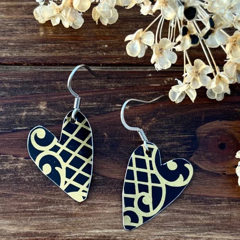 Pair of black and gold geometric heart-shaped earrings with lattice and scroll detailing.