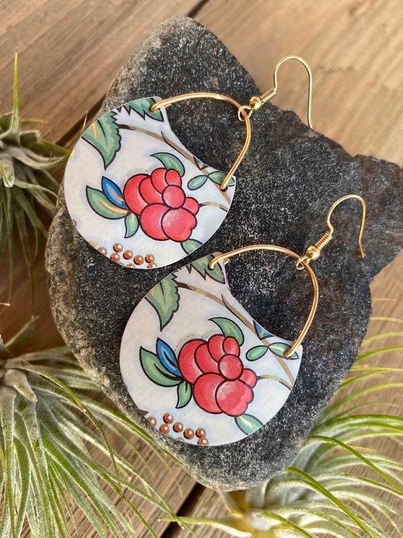 Hand-painted ceramic earrings with red berries and green leaves, mounted with gold-tone hooks on stone.