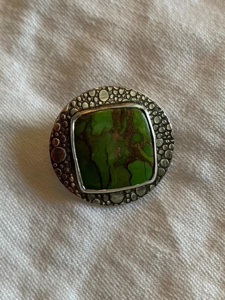 Silver ring with textured band and green stone cabochon centerpiece.