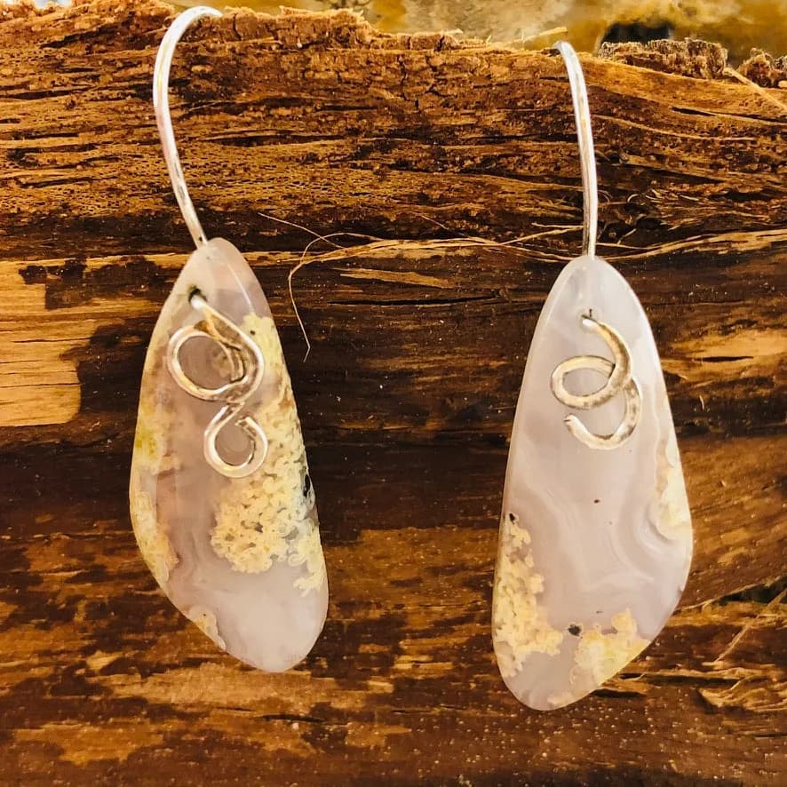 Pair of stone-slice earrings with wire-wrapped metalwork details, displayed on weathered wood.