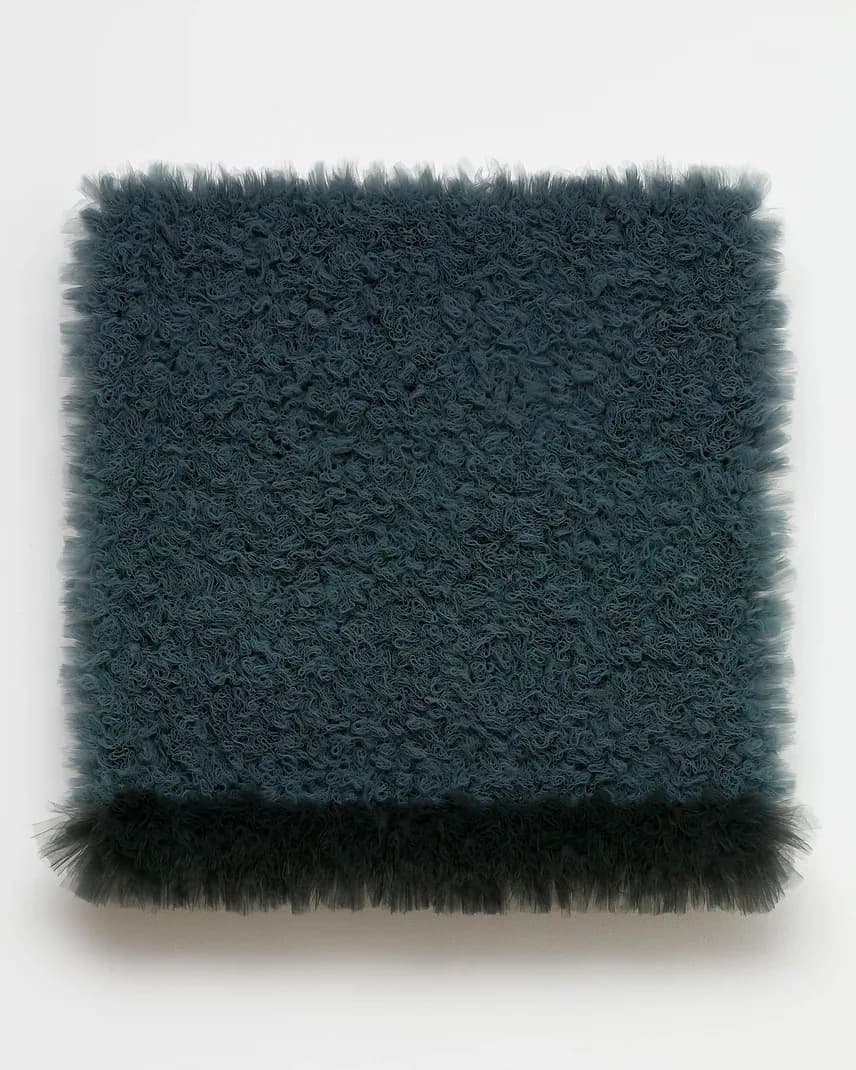 Non-representational fiber artwork with teal and black textured surfaces mounted on white wall.