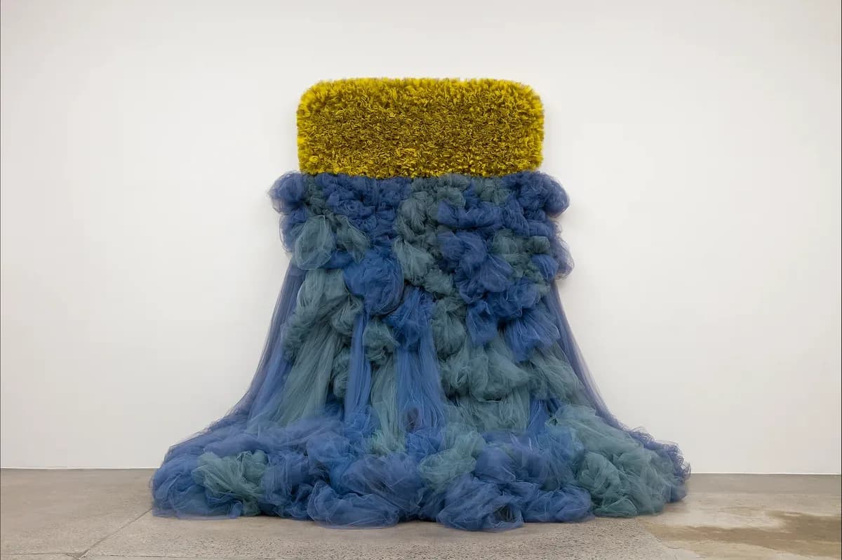 Large-scale fiber installation combining yellow textile crown and cascading blue and teal fiber forms in a gallery space.