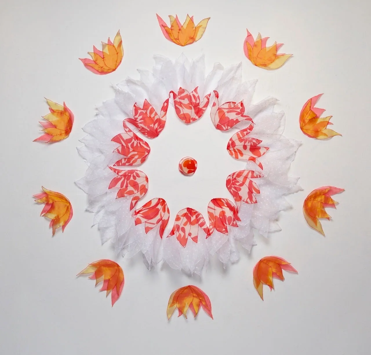 Circular composition of layered paper petals in coral, white, and gold arranged in concentric rings.