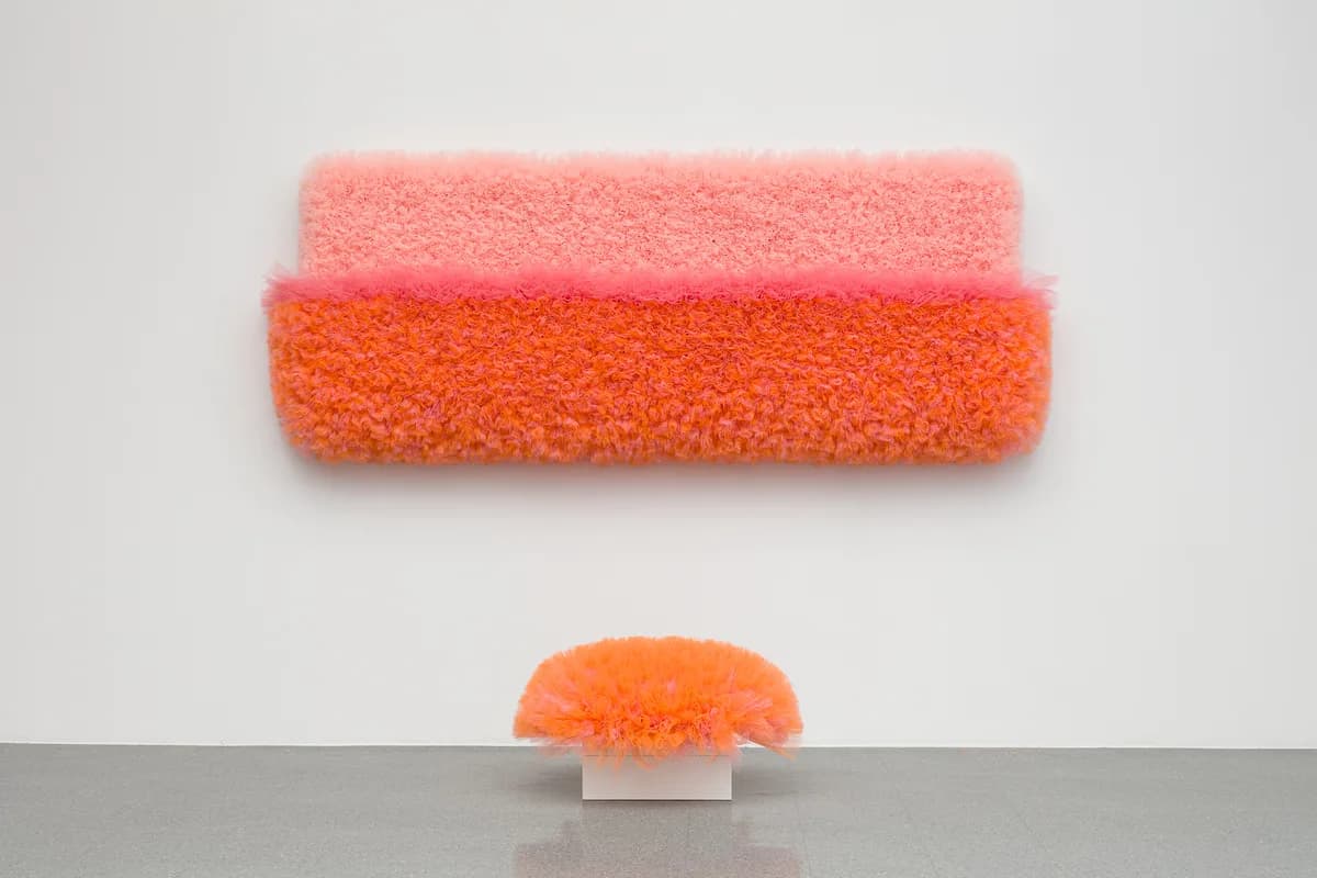 Two stacked fiber forms in coral and orange tones with a smaller hemispherical element below, arranged on a white and gray surface.