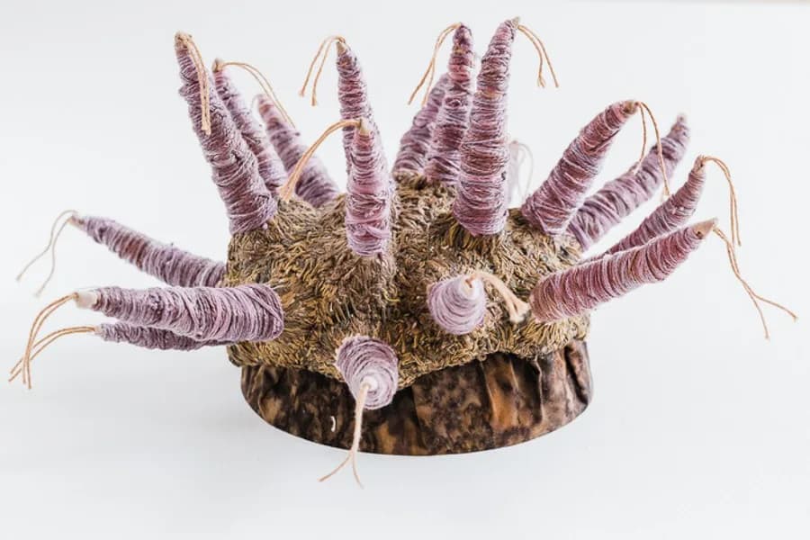 Fiber and textile sculpture with purple wrapped strands, woven base, and organic spindly forms.