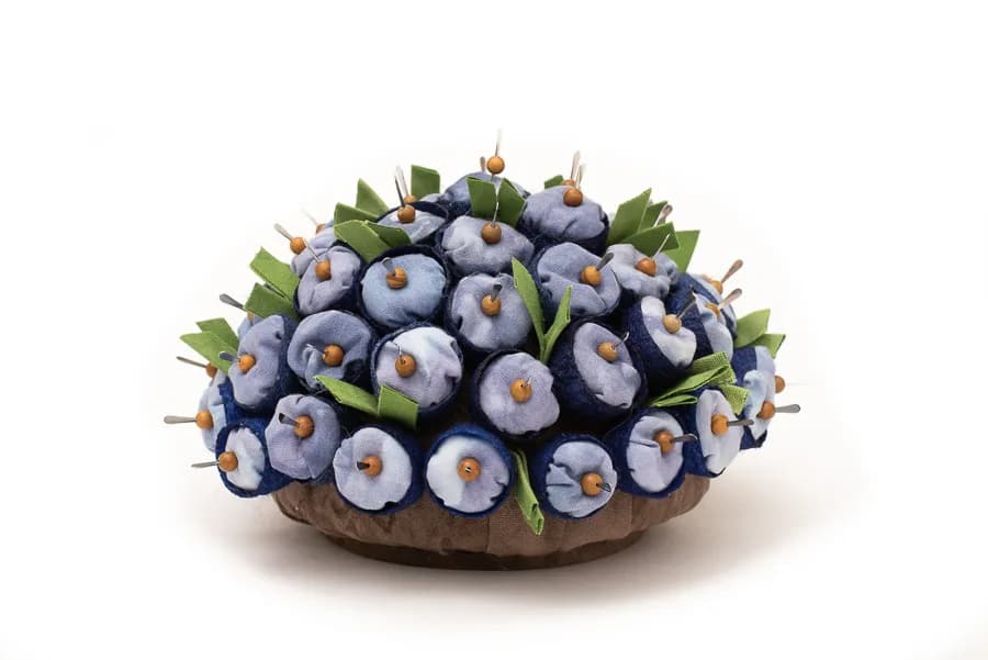 A dense, rounded cluster of ripe blueberries with green leaves in a shallow wooden bowl.