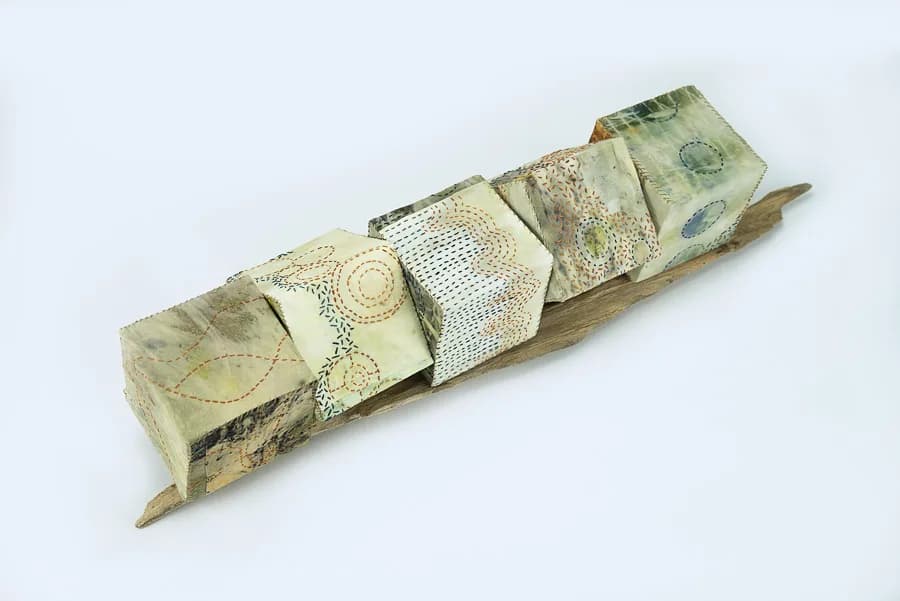 A sculptural book art piece with folded handmade pages bearing intricate pen drawings and patterns mounted on weathered wood.