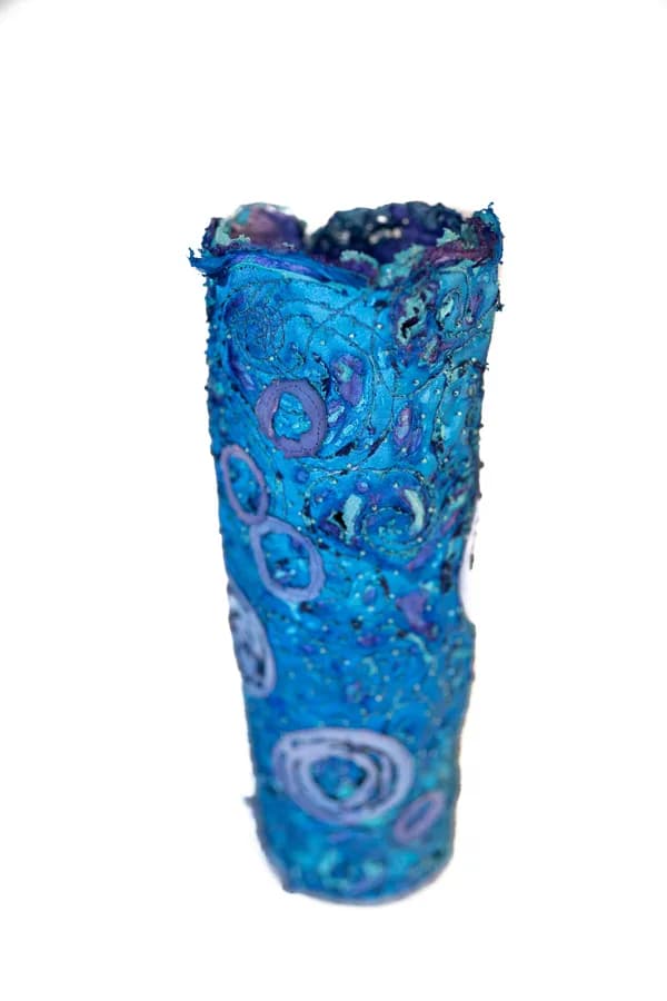 A freeform blue glass vessel with textured organic surface and layered circular patterns.