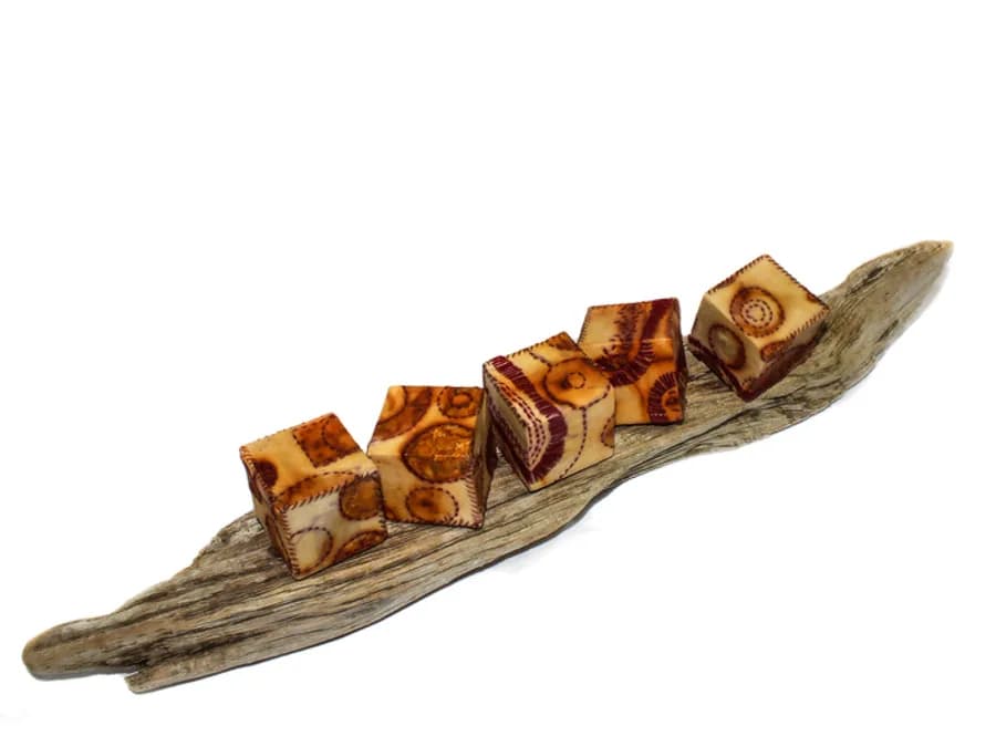 Handmade wood beads with pyrography patterns arranged on a driftwood base.