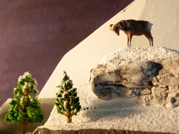 A small deer stands atop a sculpted stone landscape with miniature trees and shadowed rock formations.