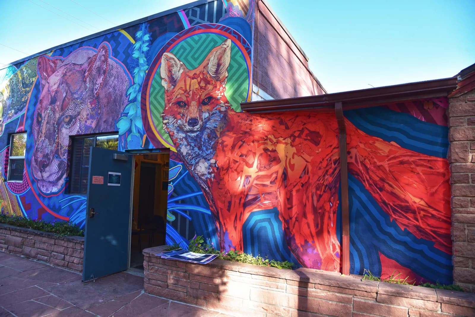 Large-scale exterior mural featuring a fox and abstract wildlife imagery in vibrant blues, purples, and reds.