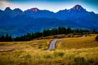 Winding road cuts through alpine meadow beneath the Boulder Flatirons and distant peaks.