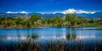 Reflective marsh landscape with snow-capped Boulder Flatirons rising beneath a clear blue sky.