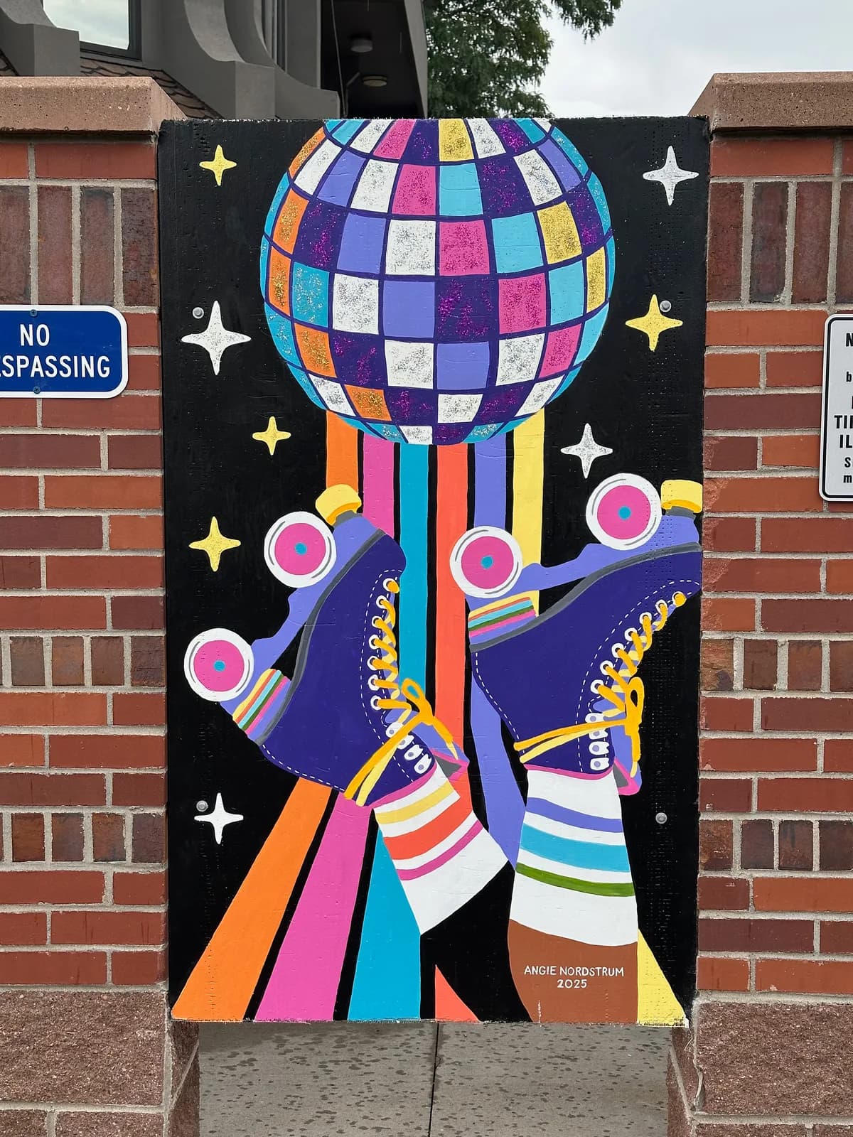 A vibrant public mural depicting retro roller skates and a colorful disco ball against a black background.