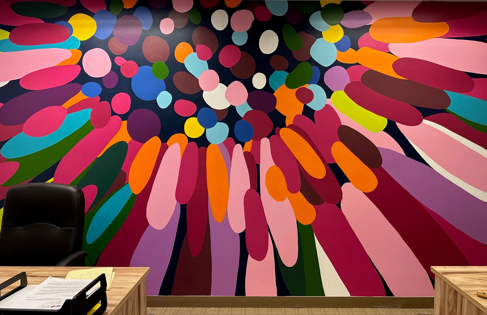 A vibrant large-scale mural featuring overlapping geometric shapes in bold pinks, oranges, blues, and greens.