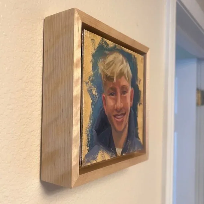 Photorealistic portrait of a smiling woman rendered with gold leaf and mixed media in a wood frame.