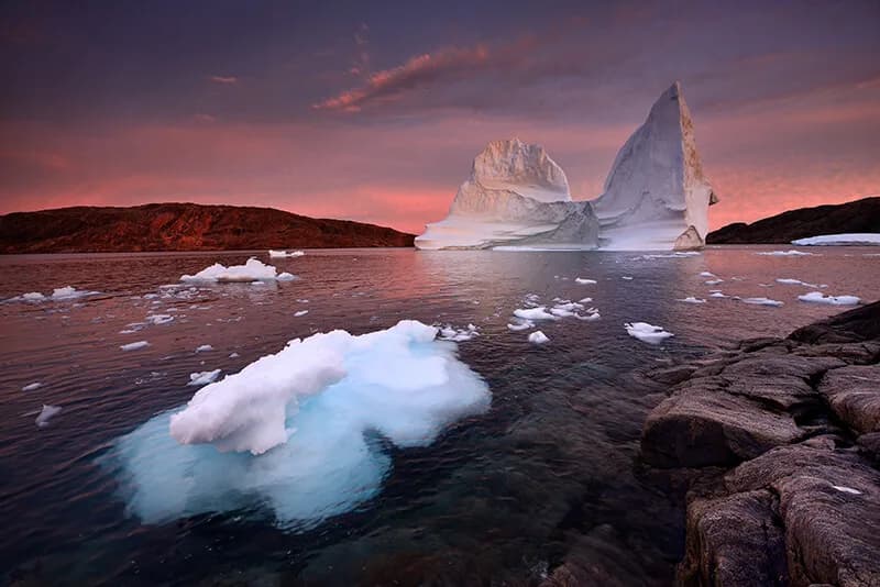 Arctic icebergs and glacial formations lit by a purple-pink twilight sky in this panoramic landscape photograph.