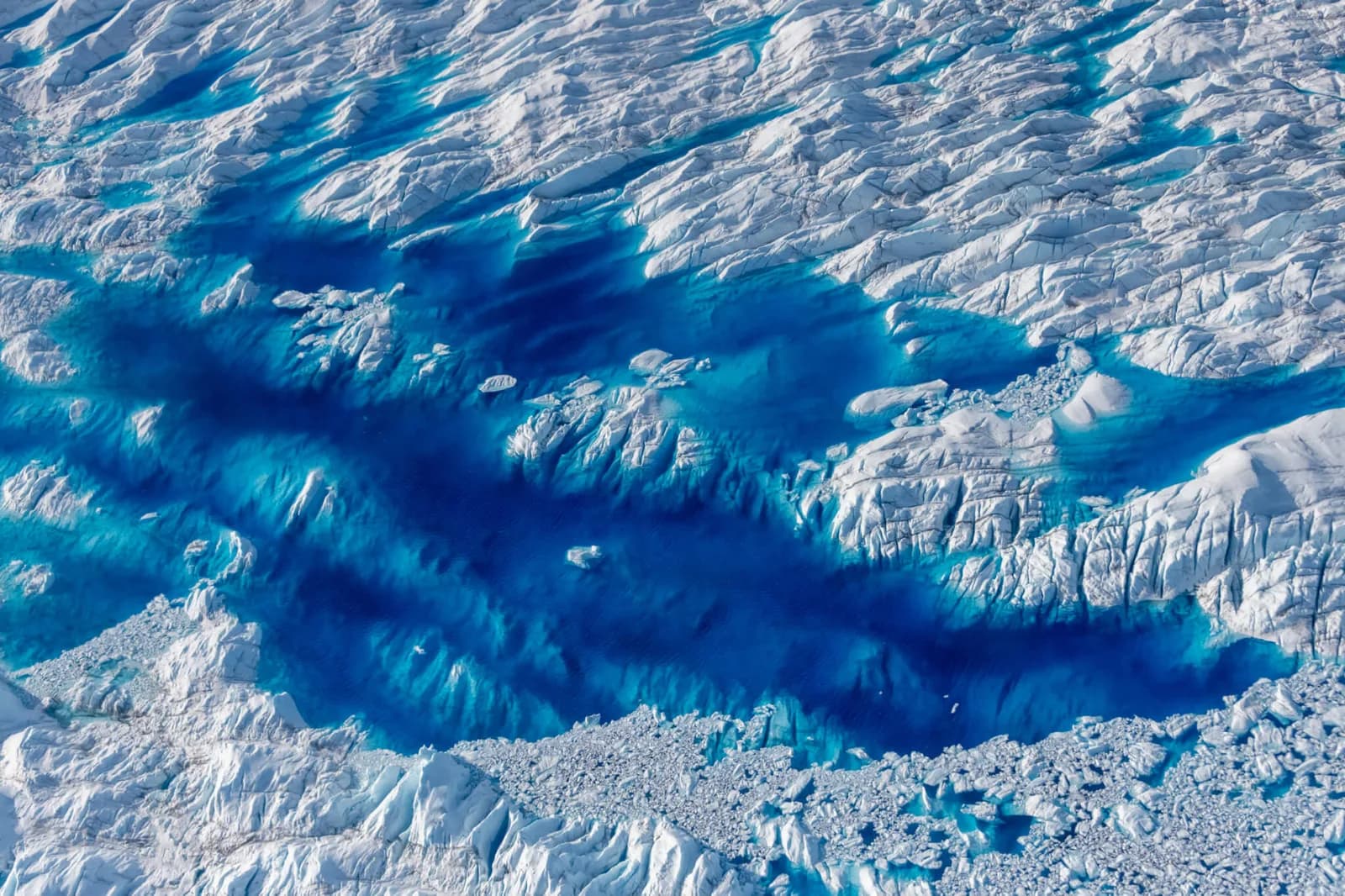 Aerial photograph of a glacial landscape with white peaks and vivid turquoise meltwater channels.