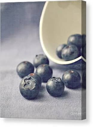 Blueberries scattered near a ceramic bowl captured in soft, cool-toned still-life photography.