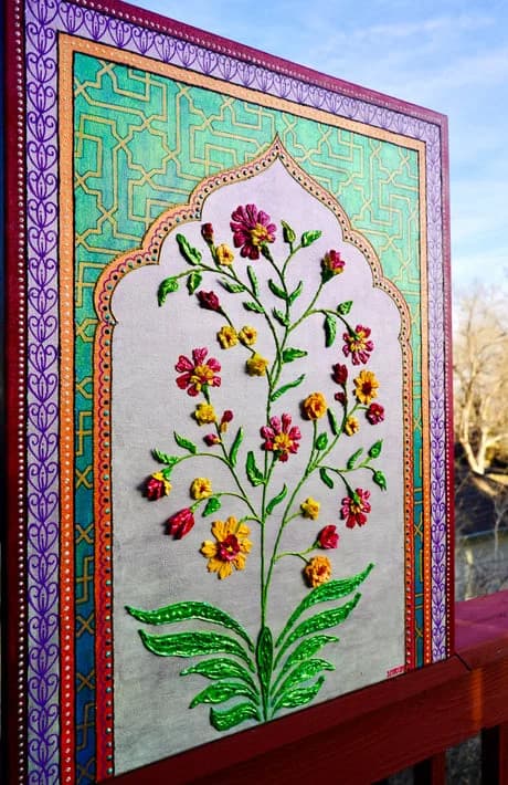 Hand-embroidered floral textile with red, yellow, and purple flowers on cream fabric, set in ornate frame.