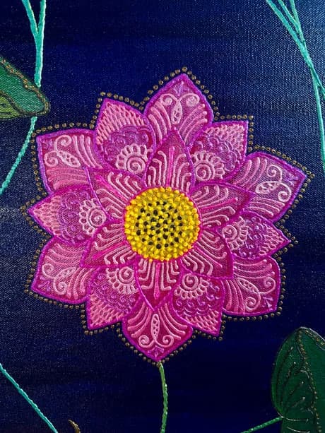 Embroidered and beaded magenta flower with ornate patterning on dark blue textile.