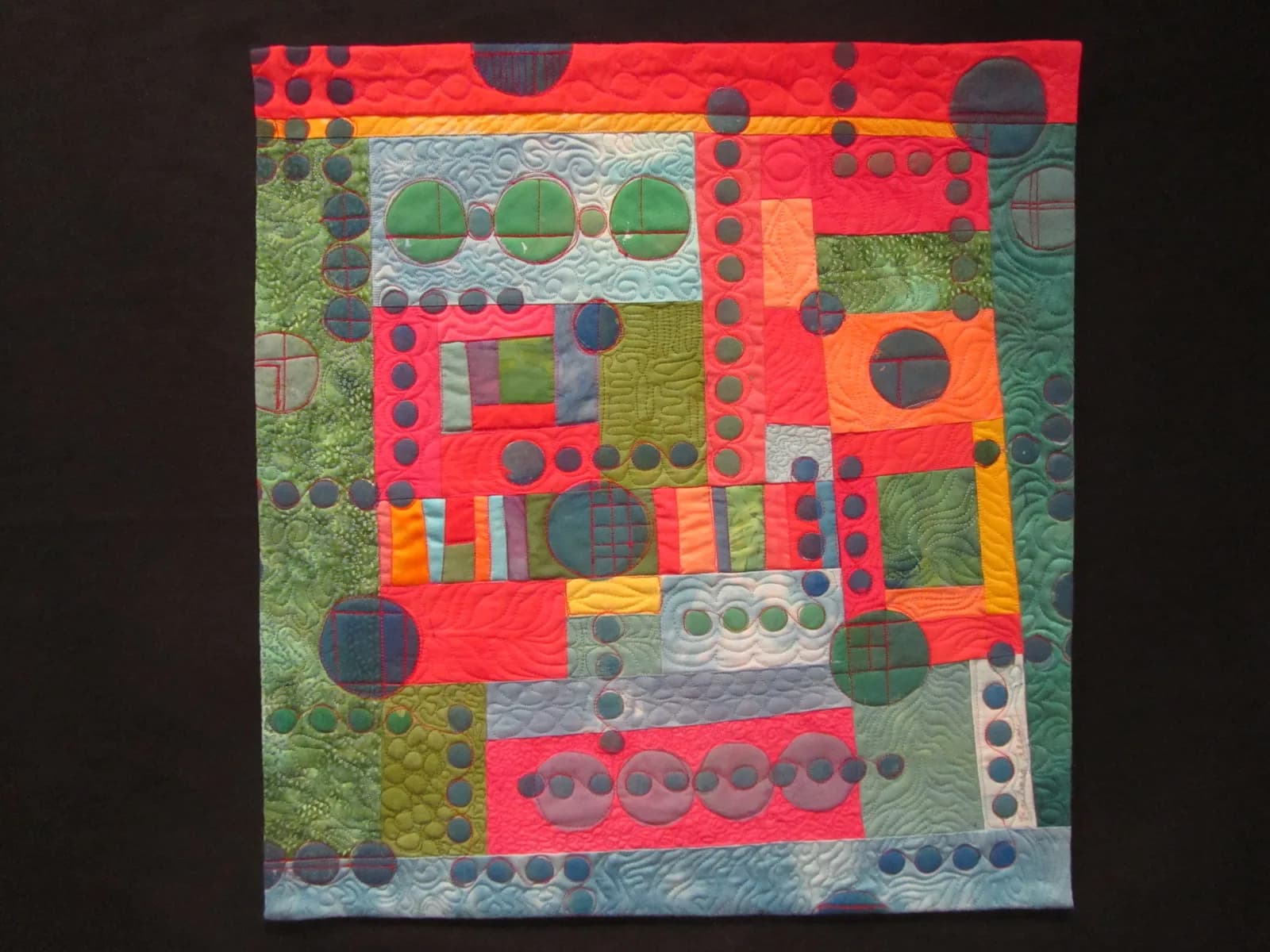 Abstract quilted textile featuring bold red, green, and yellow geometric forms with textured circles and layered stitching.