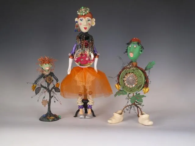 Three hand-sculpted ceramic figures with beaded embellishments and mixed materials arranged in a group composition.