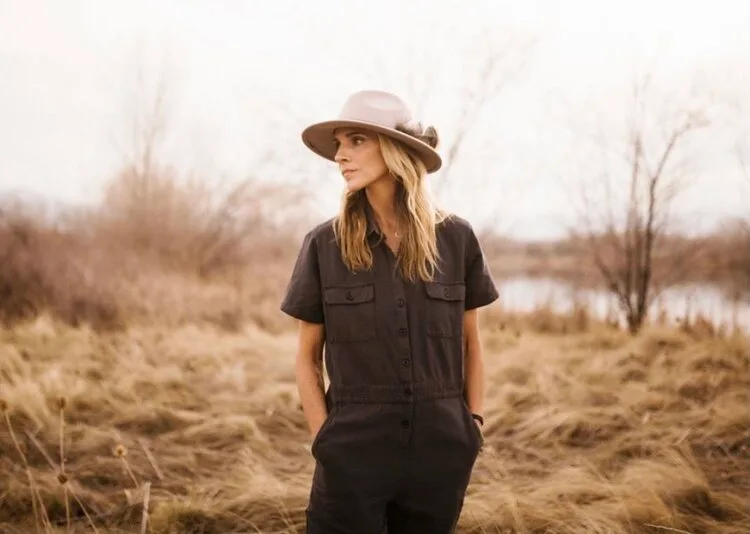 Posed portrait of a person wearing a hat in an outdoor landscape setting.