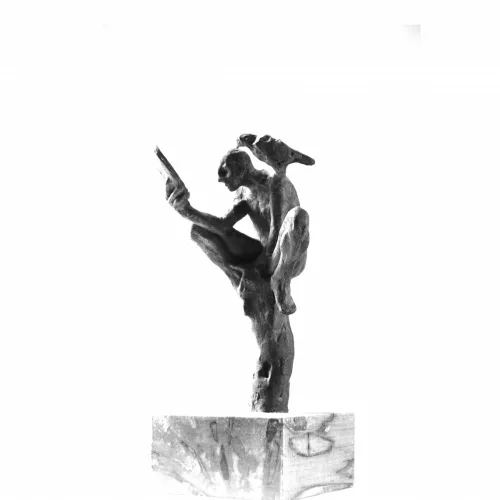 A cast bronze monkey sculpture perched in a playful pose, examining something in its hand.