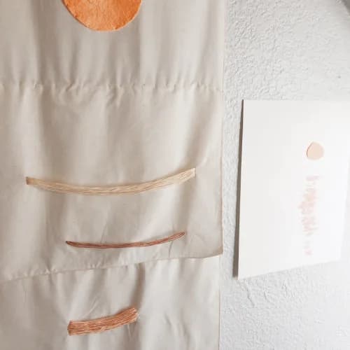 Abstract textile composition combining natural fiber strips and a copper circle on cream linen.