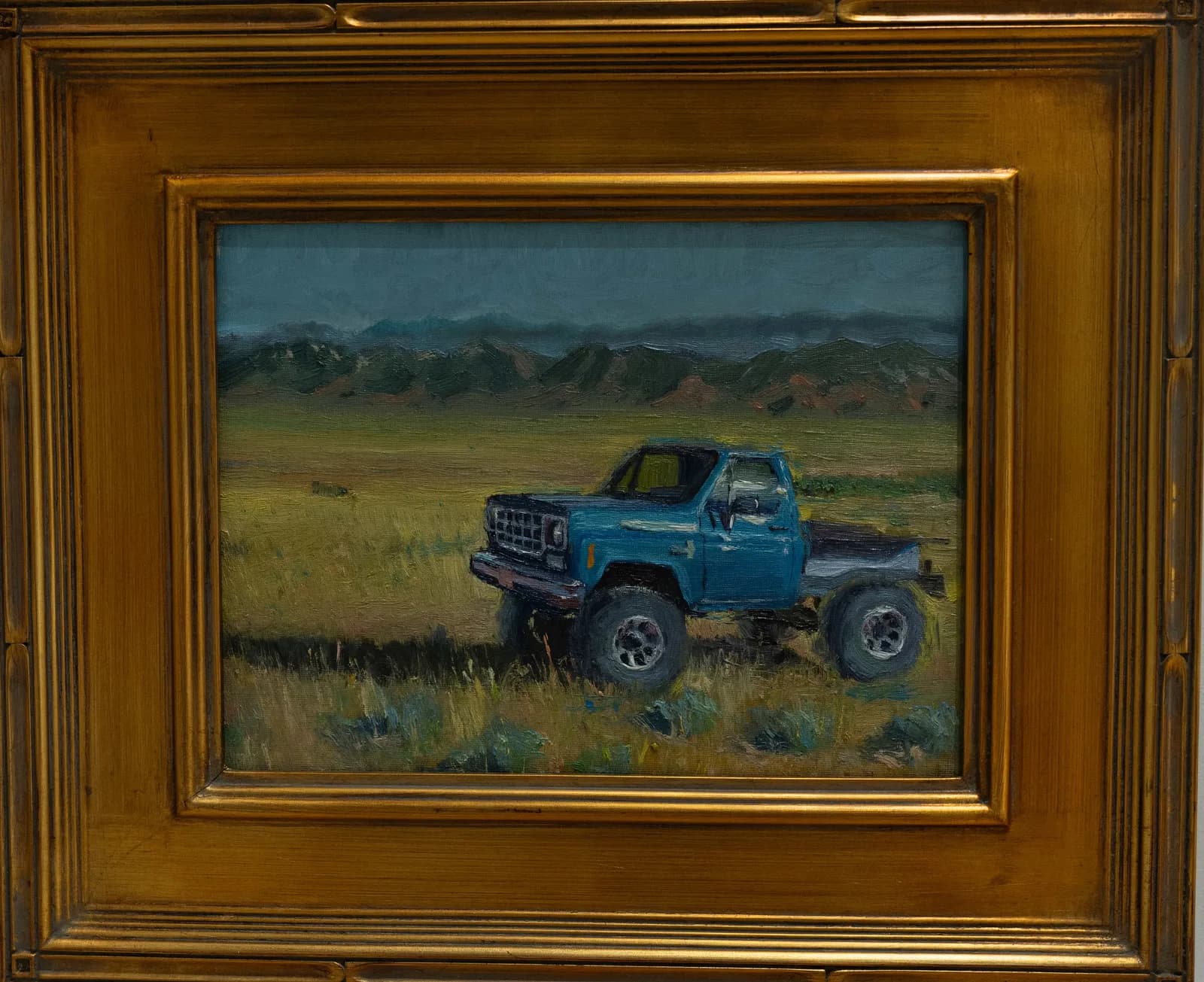 A lifted blue truck abandoned in an arid high-desert grassland beneath distant mountains.