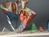 Abstract welded metal sculpture with dynamic angular forms and warm tones against a gray wall.