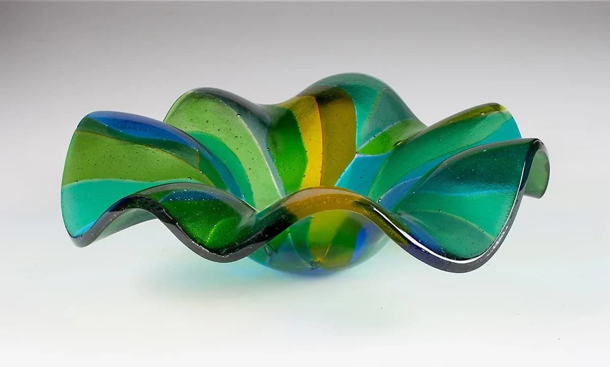 Undulating glass sculpture in layered greens, blues, and yellows with organic wave-like form.