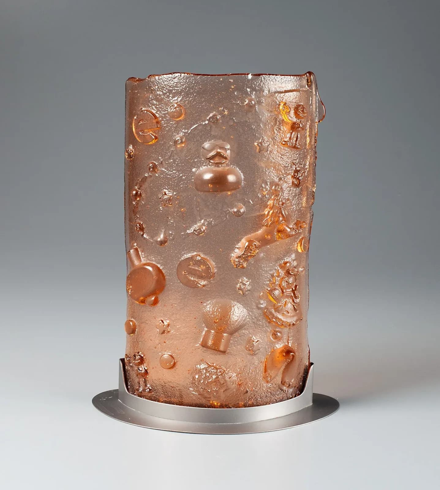 Bronze sculptural vessel with embedded portrait head and relief elements mounted on a metal base.