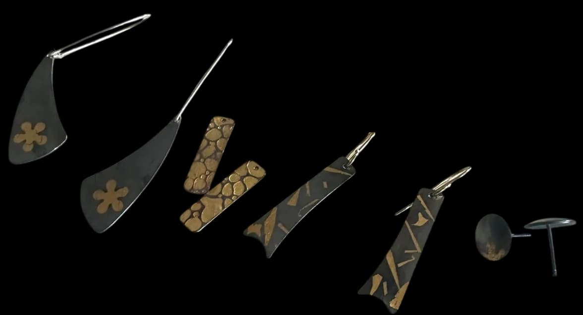 A collection of handcrafted metal jewelry pieces with inlaid enamel and decorative patterns on a dark background.