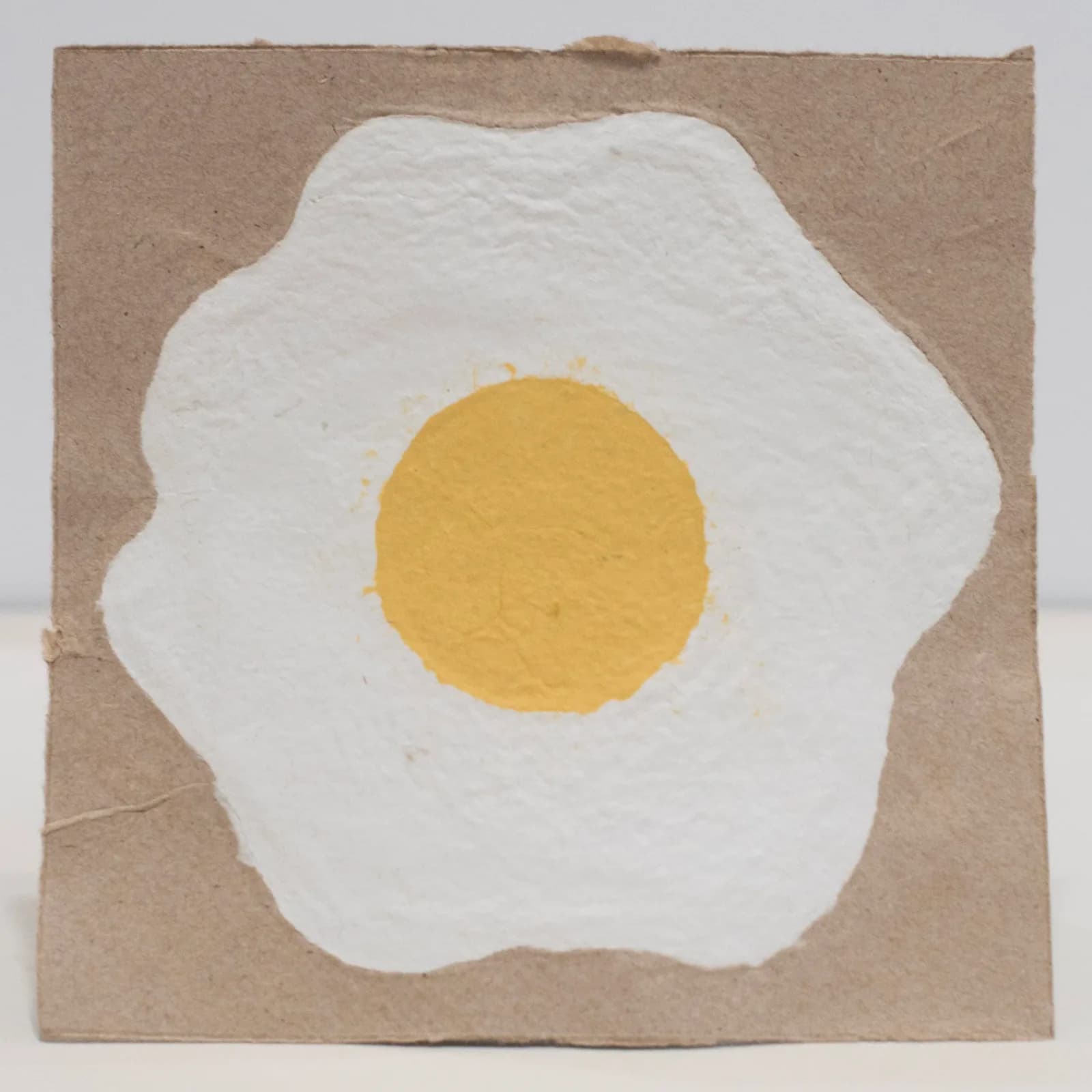 A white organic circle with yellow center on tan paper, painted with expressive edges.