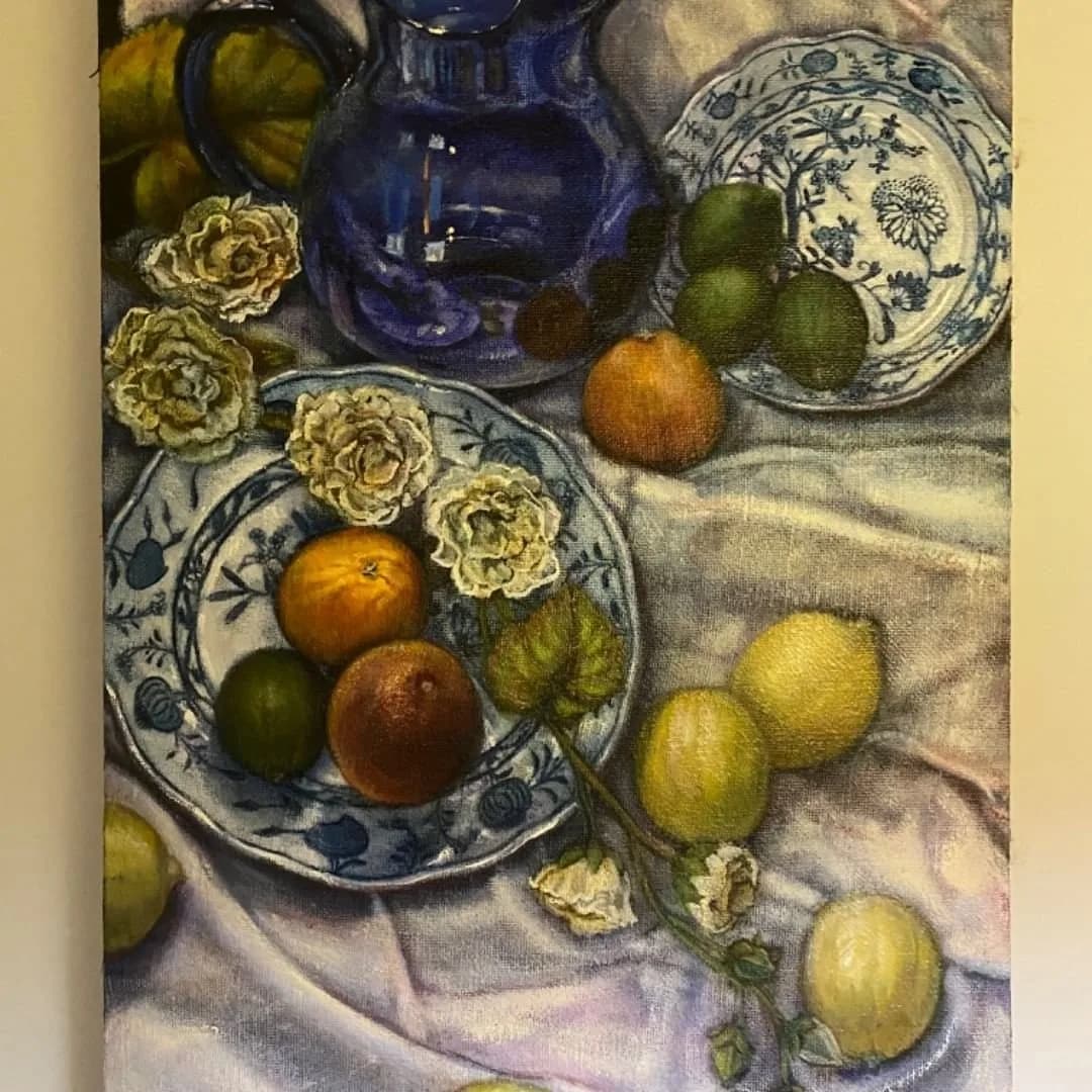 Still life composition with citrus fruit, cream-colored roses, and blue and white ceramic plates on draped fabric.