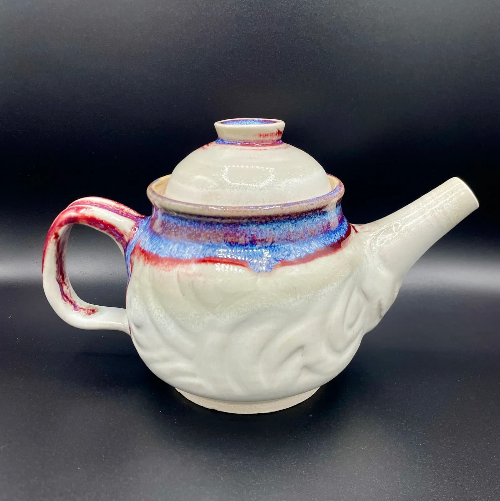 Hand-formed ceramic teapot with cream glaze, red and blue brushed glaze accents on the body and handle.