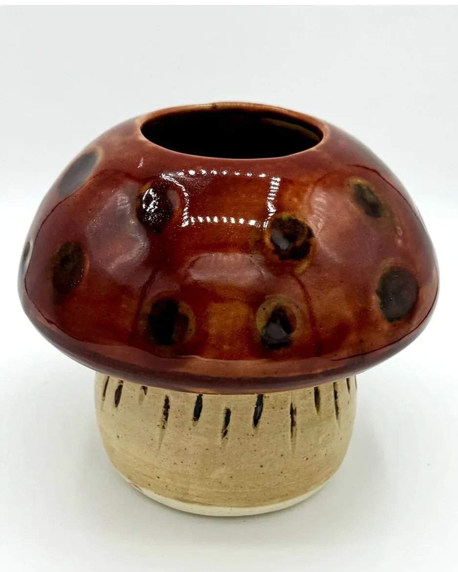 Handmade ceramic vessel in the form of a red mushroom with textured stem and decorative details.
