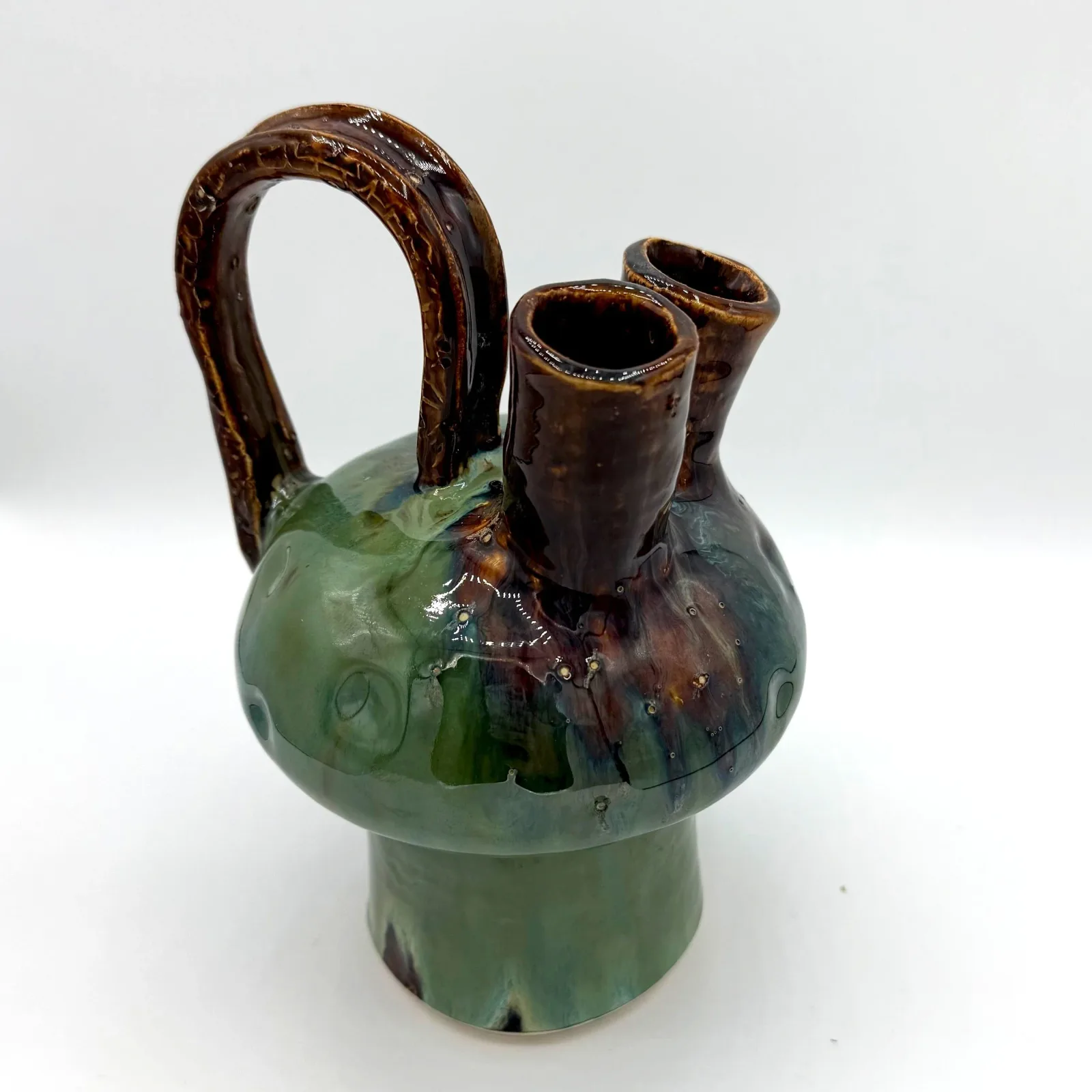 Ceramic vessel with green glaze, brown-glazed handle and spouts, handmade earthenware form.
