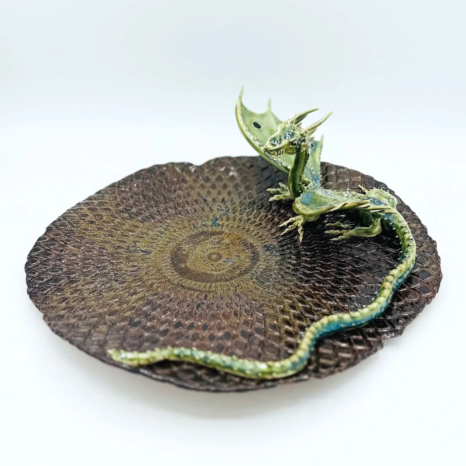 A green and bronze metal dragon sculpture rests on a textured spiral-patterned base.