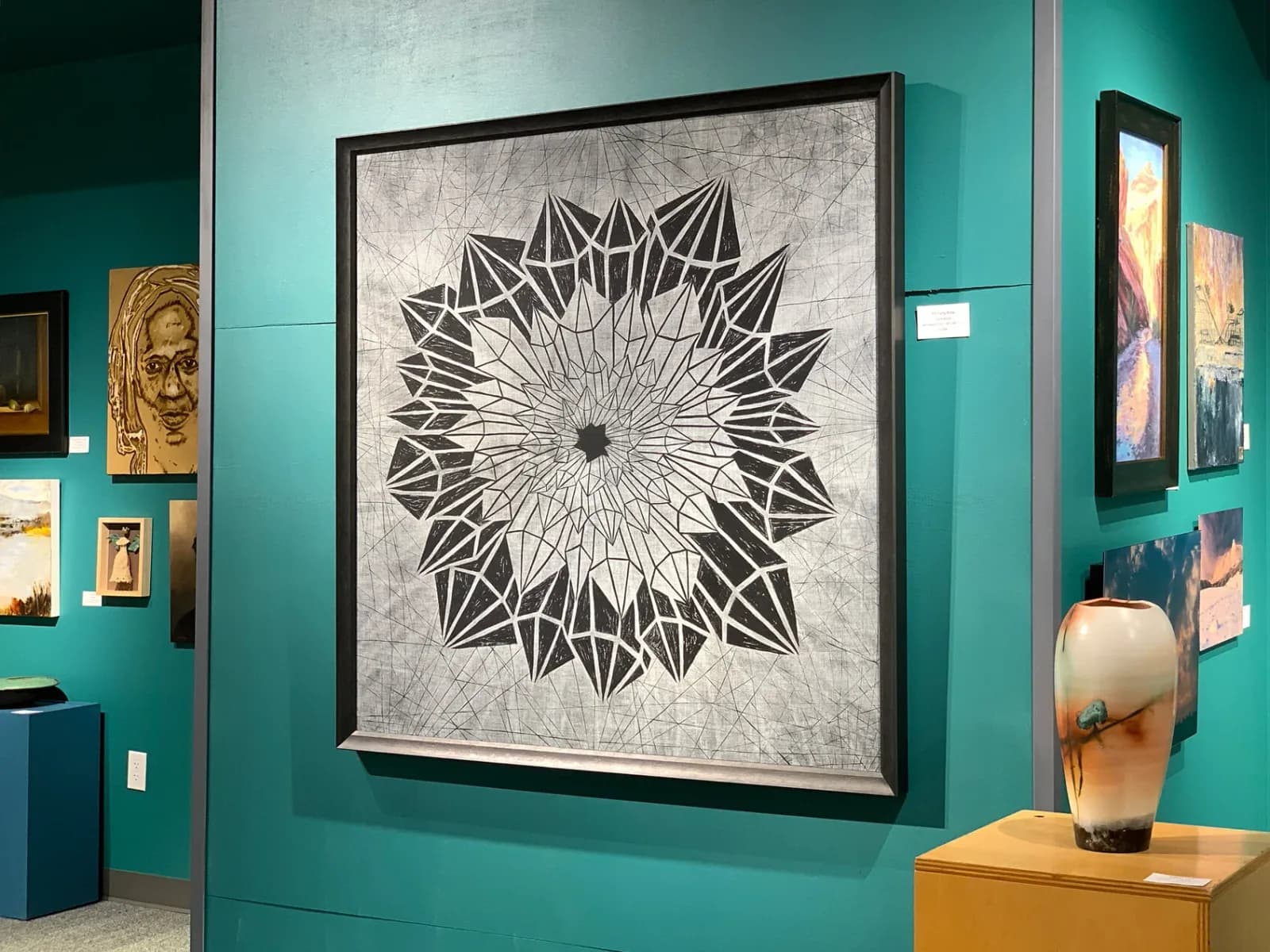 Geometric mandala with concentric triangular rays in black ink and graphite on textured paper.